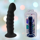 On the left side, an 8" black, ridged silicone dildo from Maia, known as 'Kendall,' stands upright against a blurred backdrop of soft, colorful lights. On the right, the same harness-compatible dildo is shown in its packaging labeled "Maia 'Kendall' 8" Silicone Dildo - Black.